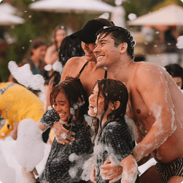 Família abraçada sendo os pais e duas filhas, estão sorrindo em uma festa da espuma no resort Salinas.