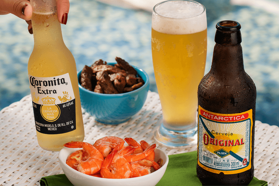 Comidas e bebidas do All Inclusive servidas ao lado da piscina, incluindo porção de camarões, fritas, quiches, um drink e cerveja gelada.