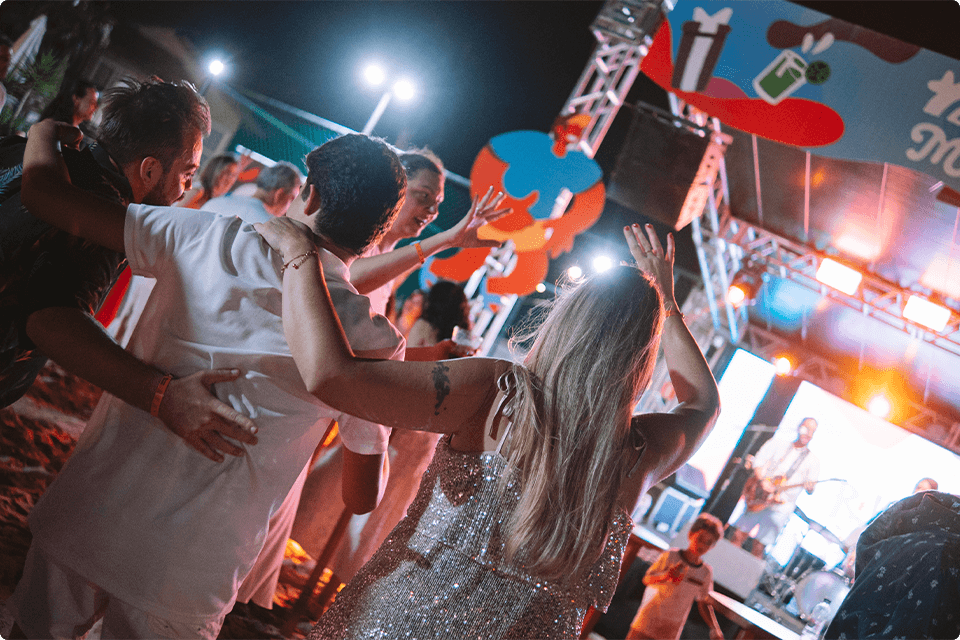 Pessoas dançando e se divertindo na festa de Réveillon do resort. O palco colorido no fundo, com a marca do Salinas Macéio.