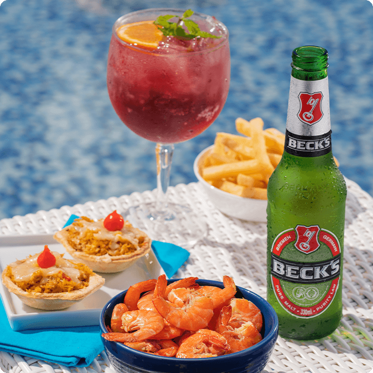 Comidas e bebidas do All Inclusive servidas ao lado da piscina, incluindo porção de camarões, fritas, quiches, um drink e cerveja gelada.
