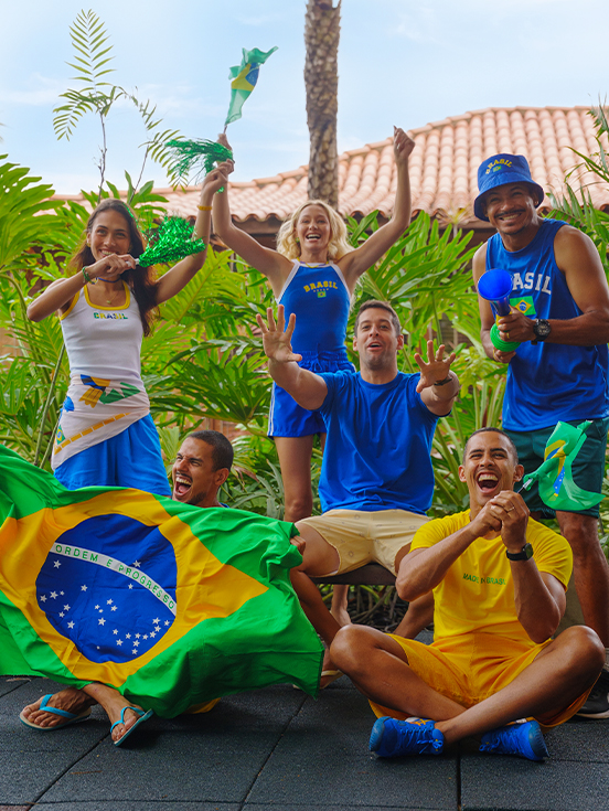 Grupo de quinto amigos torcedores usando camisas do Brasil, segurando bandeiras e vuvuzela em clima de jogo no Salinas Maceió.