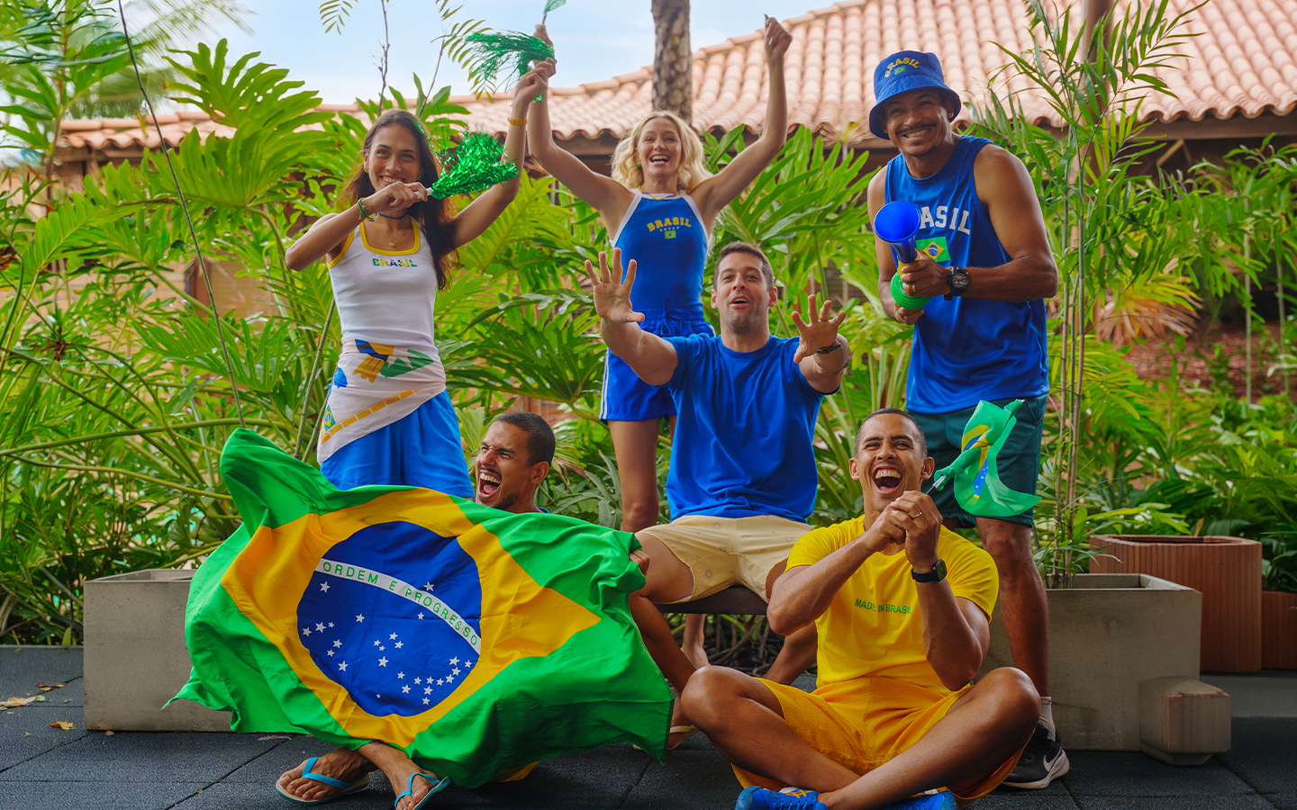 Grupo de quinto amigos torcedores usando camisas do Brasil, segurando bandeiras e vuvuzela em clima de jogo no Salinas Maceió.