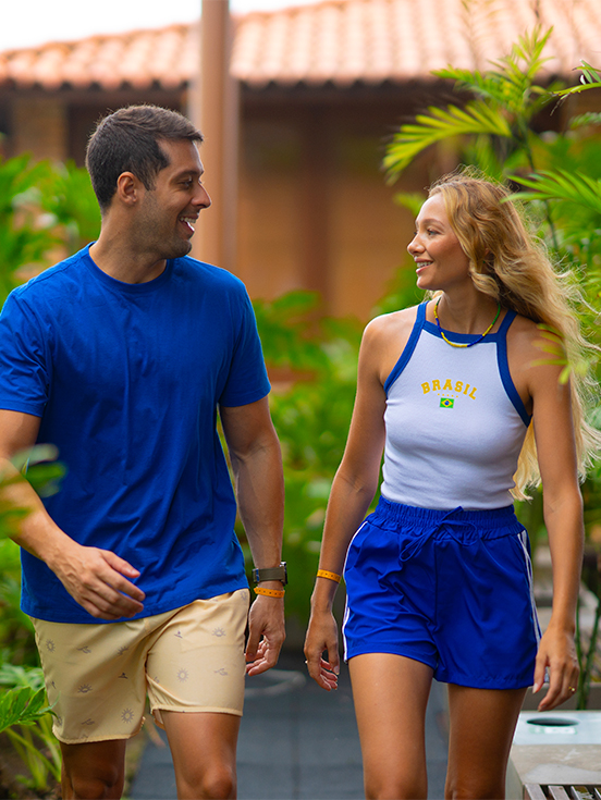 Casal caminhando sorridente em área externa do Salinas Maceió vestindo roupas nas cores azul e branco com a palavra escrita Brasil.