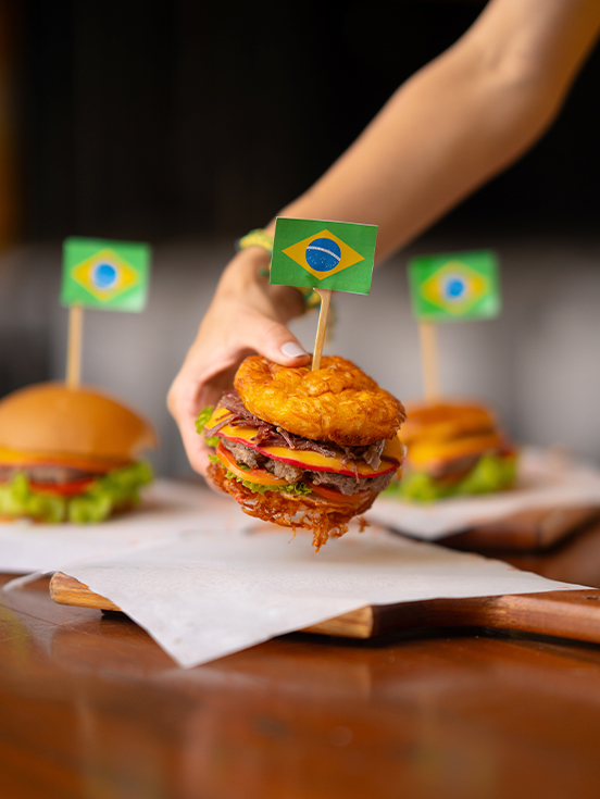 Hambúrguer pra torcida pelo Brasil no Salinas Maceió Hambúrguer artesanal com bandeira do Brasil no topo, servido em tábua de madeira no Salinas Maceió.