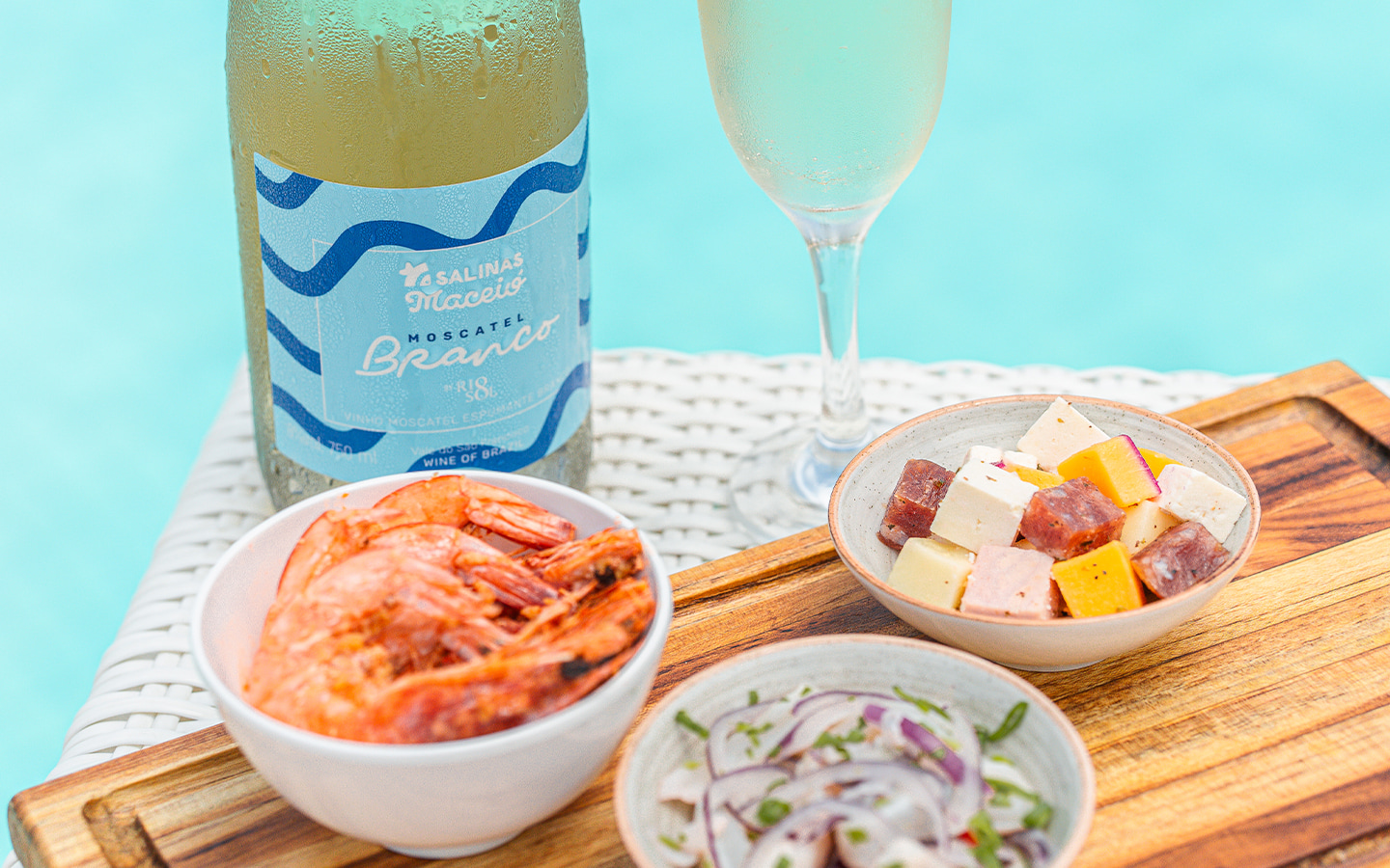 Resort All Inclusive pra família A garrafa de Moscatel do Salinas Maceió com taça ao lado. Petiscos como camarão, ceviche e queijos variados à beira da piscina.