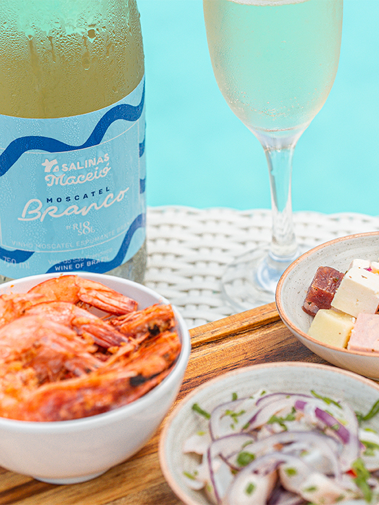 Resort All Inclusive pra família A garrafa de Moscatel do Salinas Maceió com taça ao lado. Petiscos como camarão, ceviche e queijos variados à beira da piscina.