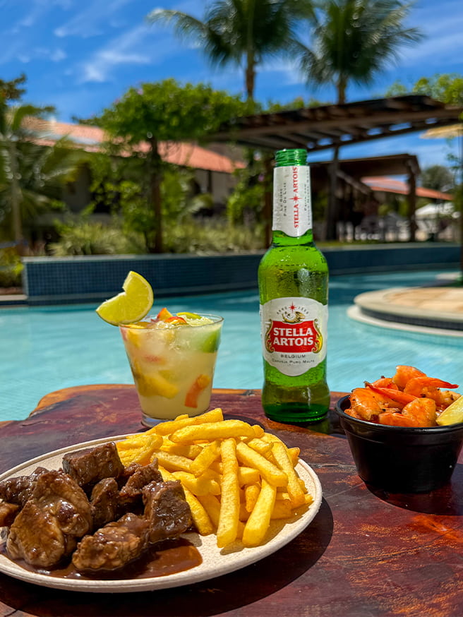 Prato com batata frita e carne, camarão, drink, cerveja Stella Artois servido à beira da piscina no Salinas Maceió.