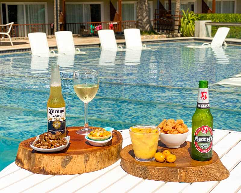 Imagem mostrando a variedade de bebidas e petiscos oferecidos pelo resort Salinas de Maceió dispostos em mesa perto da piscina.