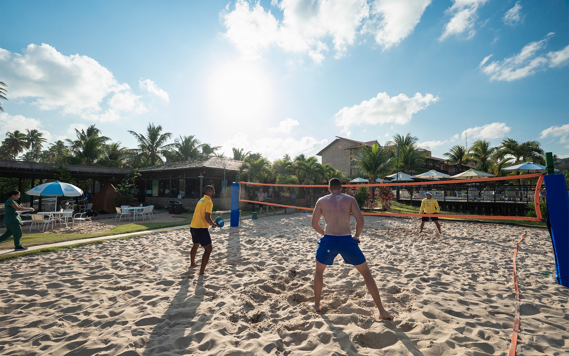 atividade-pra-todos Homens jogam vôlei, na quadra de areia montada. A dois em um time e um no outro lado da rede. Ao fundo o complexo do Salinas Maceió.
