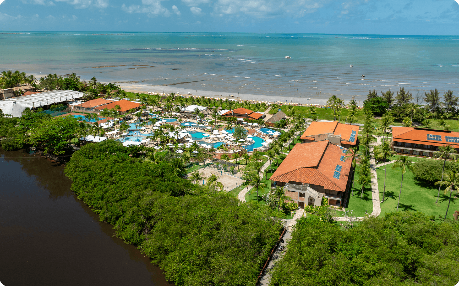 Vista áerea do complexo de piscinas do Salinas Maragogi, possível ver o espaço Cabanos, os quartos, pontos de consumo, e ao fundo a Praia de Maragogi com maré baixa.