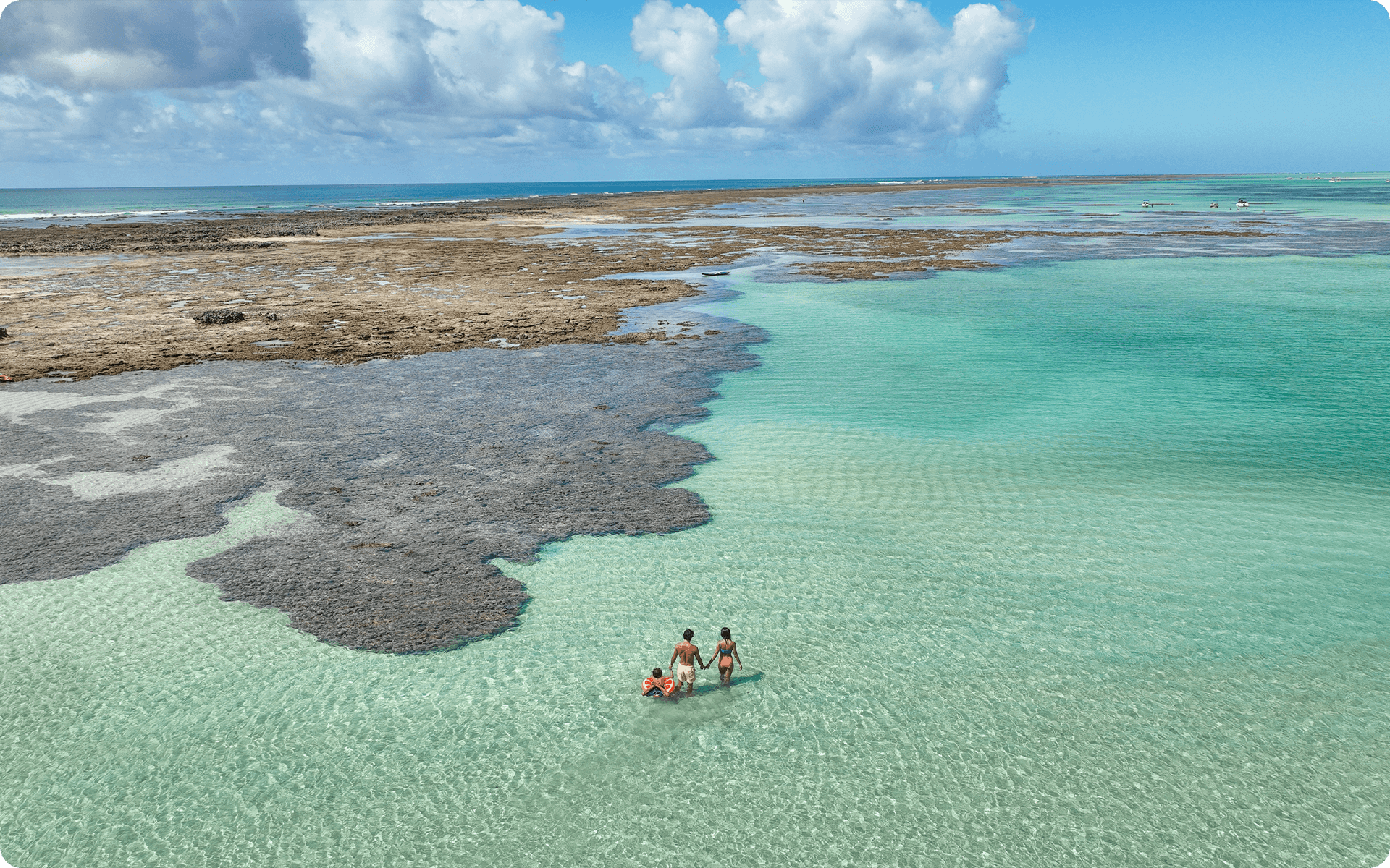 Pai, mãe e filha estão nas piscinas naturais de Ponta de Mangue, a água é cristalinas, e é possível ver os arrecifes de corais expostos.