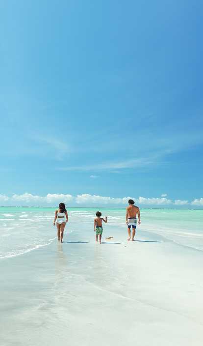 Casal e filho em Ponta de Mangue, o mar está com maré baixa e cristalino, ao fundo os arrecifes de corais.