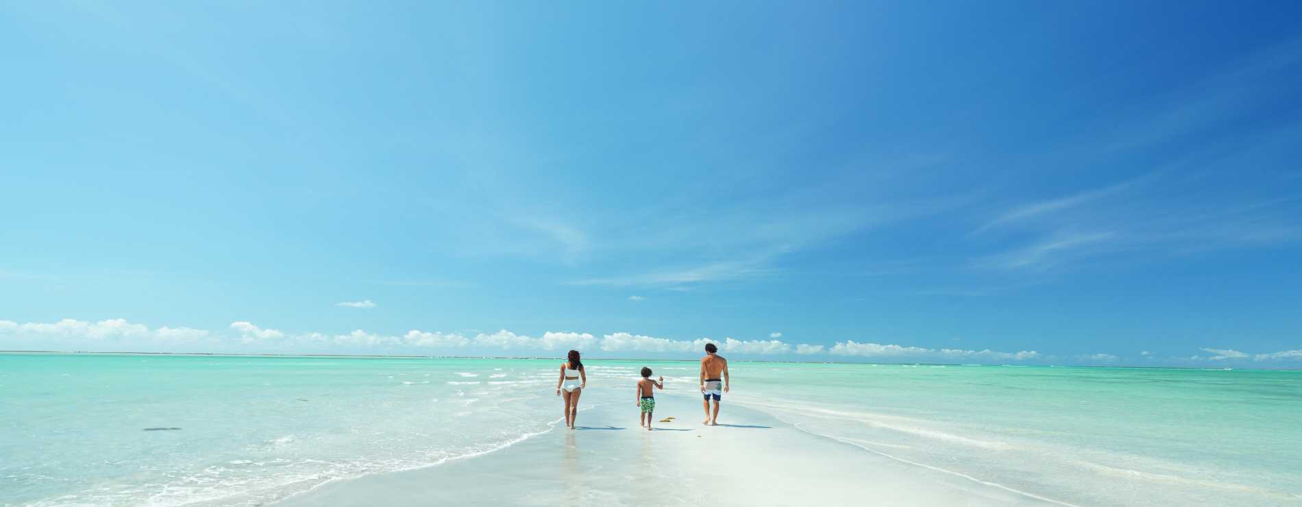Casal e filho em Ponta de Mangue, o mar está com maré baixa e cristalino, ao fundo os arrecifes de corais.