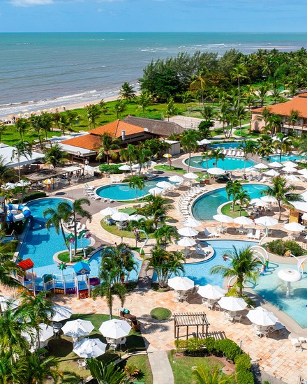 A estrutura completa do Salinas Maragogi All Inclusive Resort vista do alto. Vista aérea do Salinas Maragogi All Inclusive Resort apresentando área de lazer, piscinas, parque aquático infantil, cercados por coqueiros e vegetação litorânea, além da praia ao fundo.