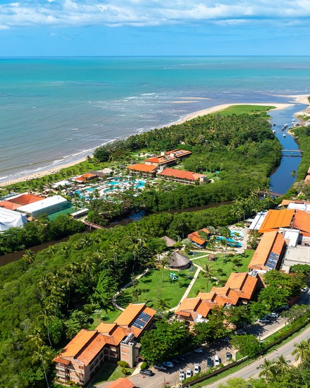 Vista aérea do Salinas Maragogi All Inclusive Resort Vista aérea panorâmica do resort Salinas Maragogi cercado por vegetação densa, com o rio a cortar a estrutura e a praia com o mar ao fundo.