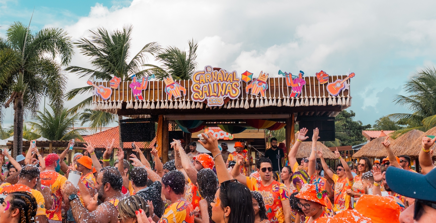Bloco de carnaval no Salinas Maragogi, com pessoas fantasiadas e curtindo, braços levantados, espuma no ar e palco decorado com temática carnavalesca ao ar livre.