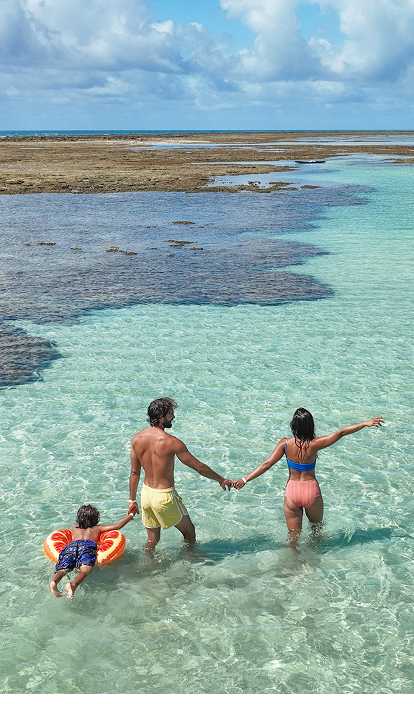 Casal e filho em Ponta de Mangue, o mar está com maré baixa e cristalino, ao fundo os arrecifes de corais.