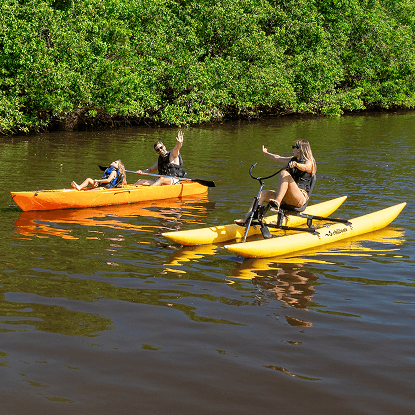 Pai e filha andando de caiaque no rio que atravessa o Salinas Maragogi, enquanto a mãe está na bicicleta aquática em dia ensolarado, sem nuvens.