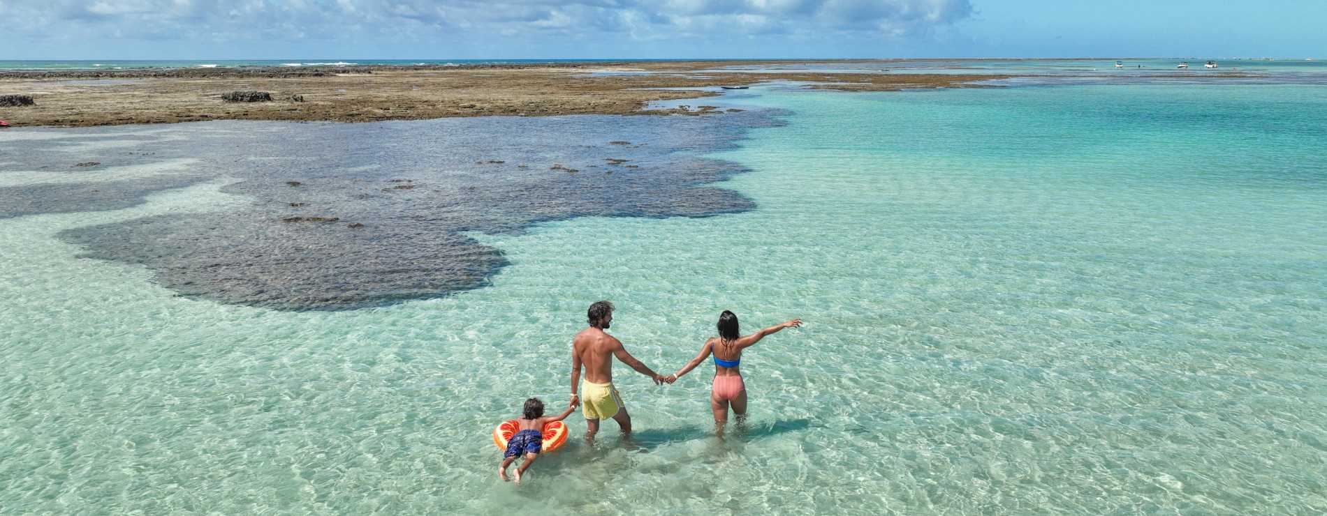 Casal e filho em Ponta de Mangue, o mar está com maré baixa e cristalino, ao fundo os arrecifes de corais.