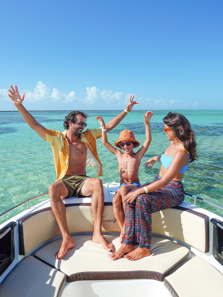 Viva momentos de pura felicidade na Praia de Ponta de Mangue Família com pai, mãe e filho alegres e comemorando de braços erguidos na proa de um barco, com as águas cristalinas da Praia de Ponta de Mangue em Maragogi ao redor.