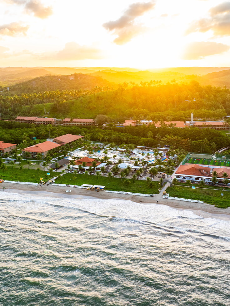 O pôr do sol que fecha o dia com chave de ouro Vista aérea do Salinas Maragogi ao entardecer, com o complexo de piscinas, praia e mata nativa ao fundo, sob céu dourado de pôr do sol.