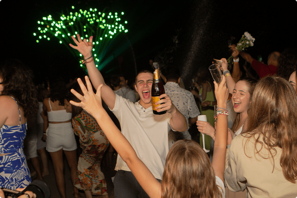 Família brindando o Reveillon com muita alegria. Taças e espumantes em mão para brindar, com fogos de artifício verde no céu.