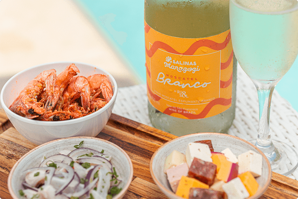 Petiscos como camarão, ceviche e queijos ao lado da garrafa de espumantes do Salinas Maragogi com taça pela metade.