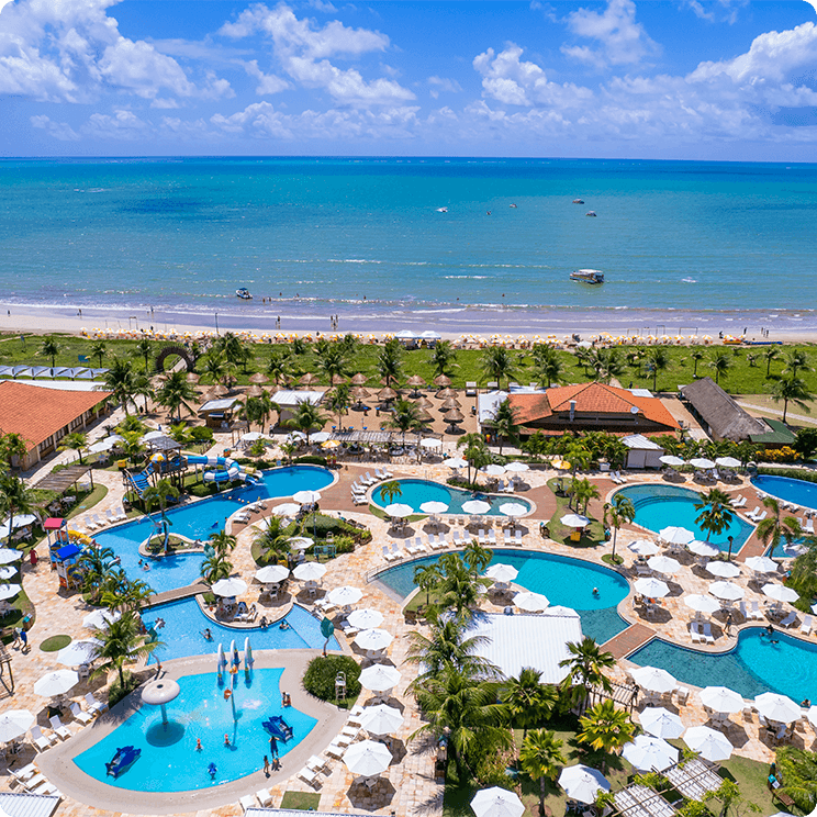 Vista aérea do Salinas Maragogi All Inclusive Resort, mostrando
a área com inúmeras piscinas, guarda-sóis brancos, alguns dos restaurantes, tudo cercado por palmeiras e está à beira-mar.