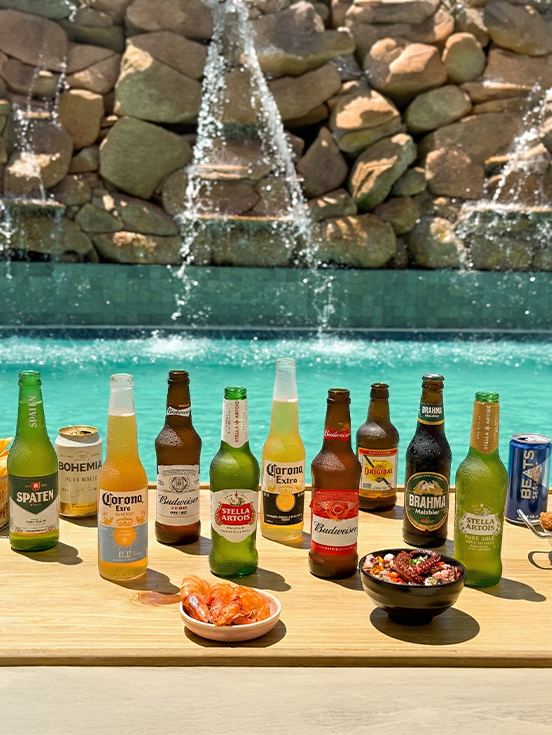 Mix de cervejas e petiscos Variedade de cervejas long neck oferecidas no resort All Inclusive Salinas Maragogi, sendo Brahma Malzbier, Corona Extra, Beats, Original, Stella Artois, Bohemia Puro Malte e Budweiser, ao lado de diversas tigelas de petiscos, sendo camarões, batatas fritas.