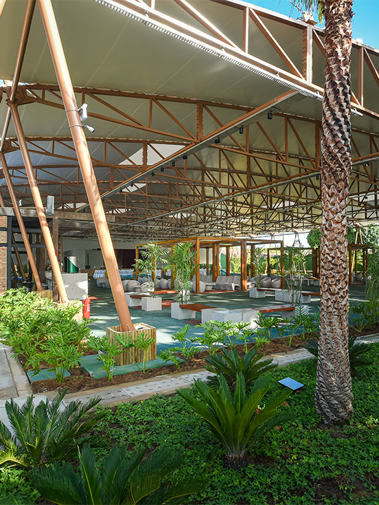 Espaço cabanos pra receber todos Ampla estrutura do Espaço Cabanos coberta com vários bancos e cadeiras, paisagismo tropical verde.