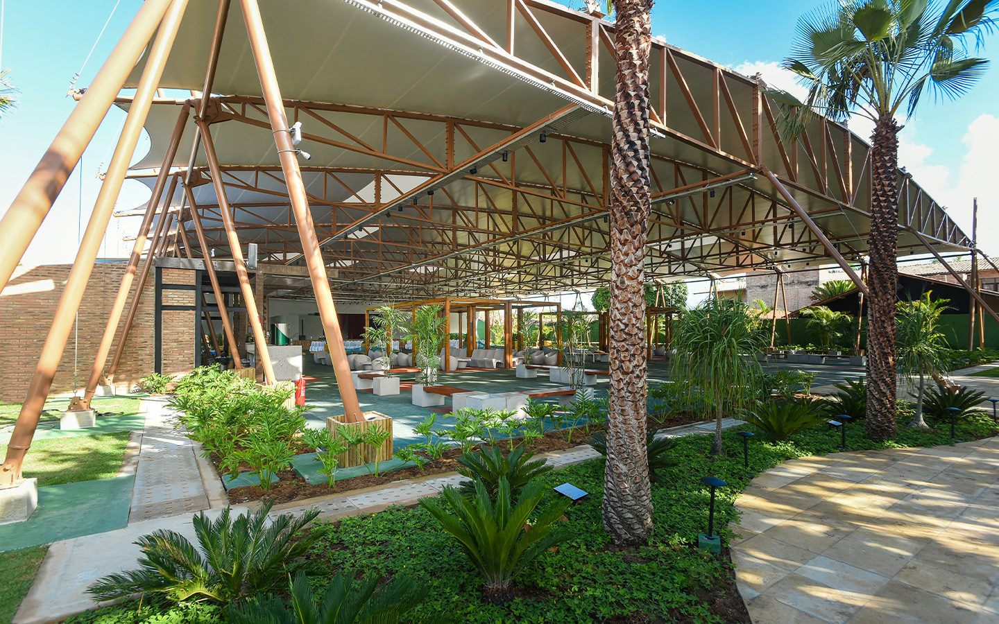 Espaço cabanos pra receber todos Ampla estrutura do Espaço Cabanos coberta com vários bancos e cadeiras, paisagismo tropical verde.