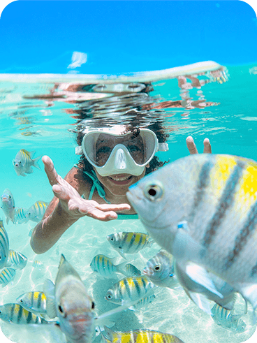 Menina nada com peixes Sargentos, típicos da costa nordestina brasileira, nas piscinas naturais de Maragogi.