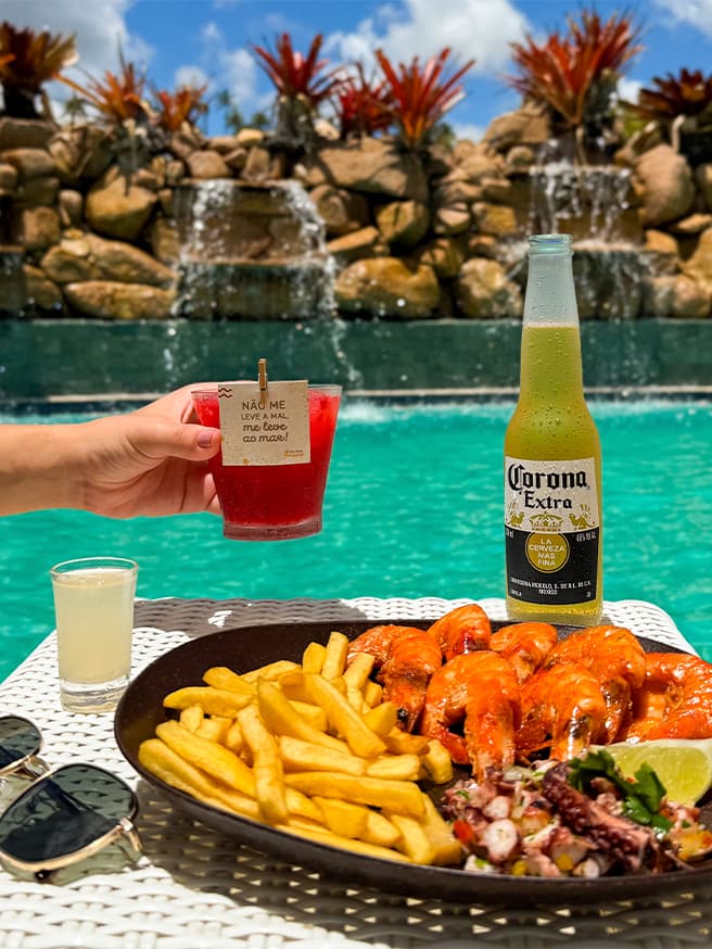 Sabor de férias é imperdível Petiscos e bebidas servidos na piscina do Salinas Maragogi All Inclusive. Com pequenas cachoeiras caindo na piscina com pedras e plantas.