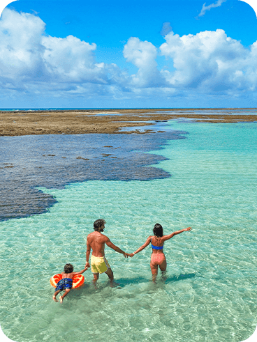 Família feliz e de mãos dadas aproveitando as águas cristalinas das piscinas naturais de Ponta de Mangue, praia próxima ao Salinas Maragogi.