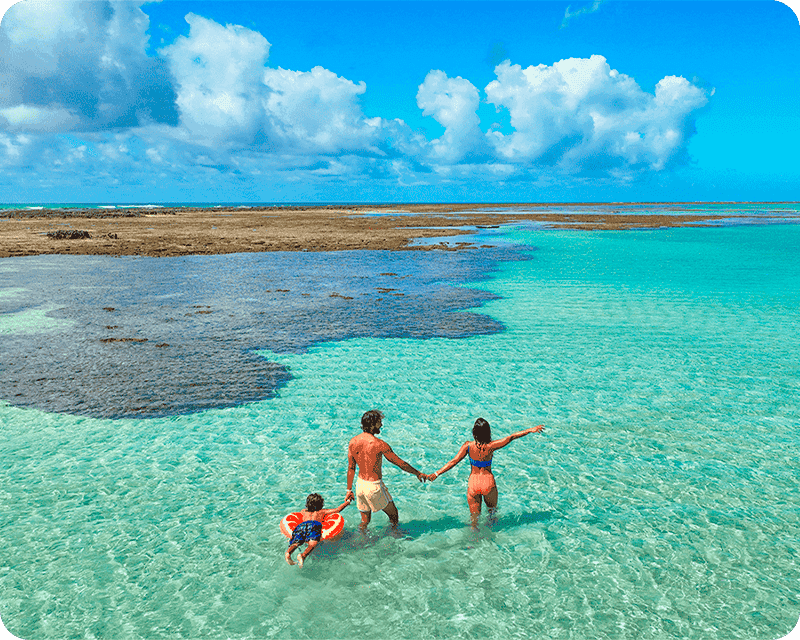 Família feliz e de mãos dadas aproveitando as águas cristalinas das piscinas naturais de Ponta de Mangue, praia próxima ao Salinas Maragogi.