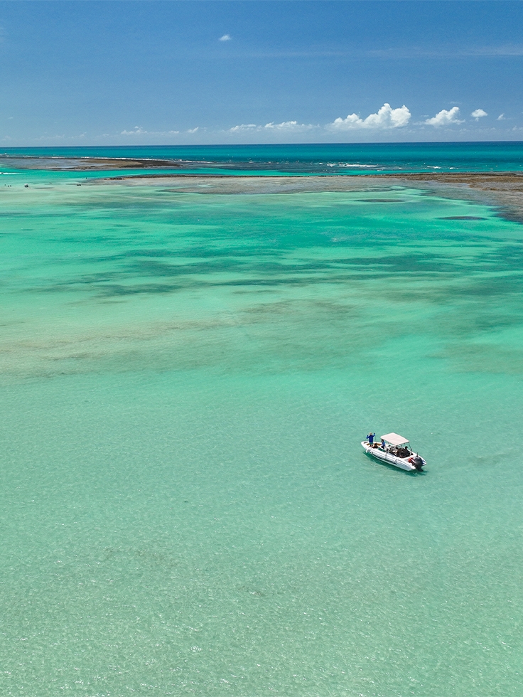 galés-de-maragogi Vista aérea das Galés de Maragogi com lancha na água azul turquesa e recifes de corais ao lado de lancha de passeio.