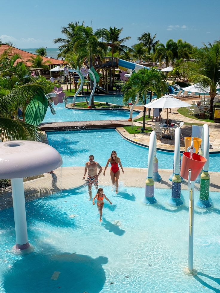 resort-pra-família-na-praia Família aproveitando brinquedos aquáticos da piscina infantil do Salinas Maragogi, com guarda-sóis e espreguiçadeiras ao redor das piscinas em dia de sol.