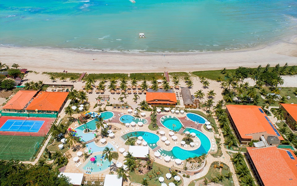 A foto mostra parte da estrutura, através de vista aéreo, do Salinas Maragogi. Localizado a beira-mar e rodeado por mata, pode-se ver o teto de alguns de seus prédios, assim como o complexo aquático composto por várias piscinas e áreas para descanso